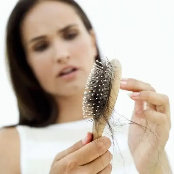 Femme examinant sa perte de cheveux sur une brosse, consultation pour soins cheveux à Nice