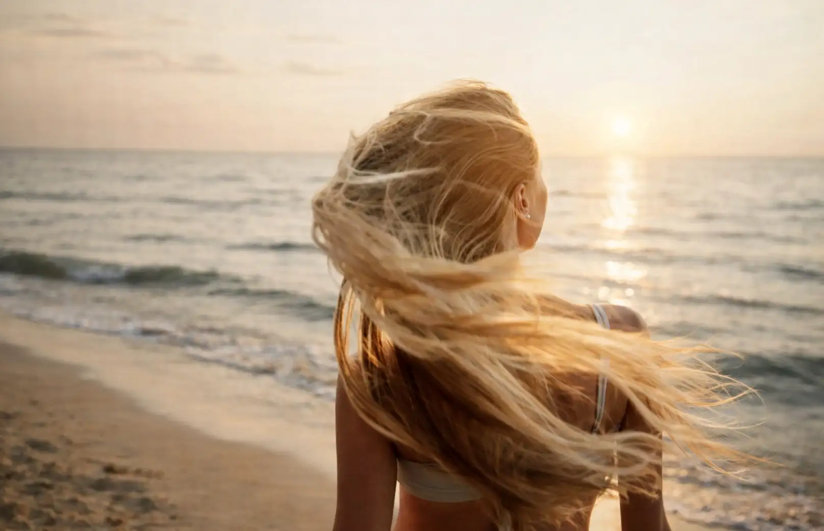 lutter contre la chute de cheveux. Femme aux longs cheveux sur une plage de Nice, profitant de la brise marine au coucher du soleil.