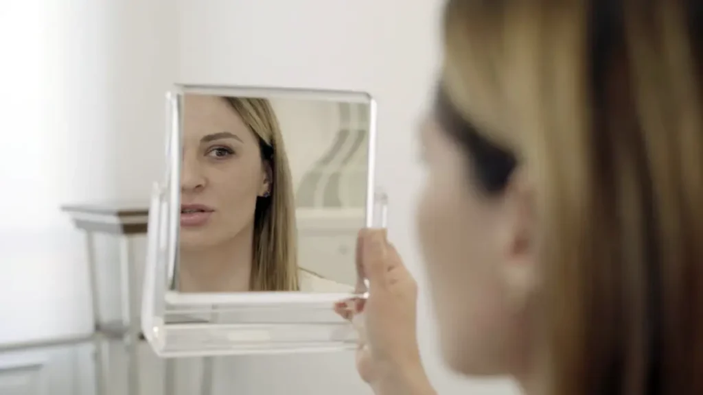 Femme observant la fermeté et l'éclat de son visage dans un miroir après un traitement esthétique non invasif.